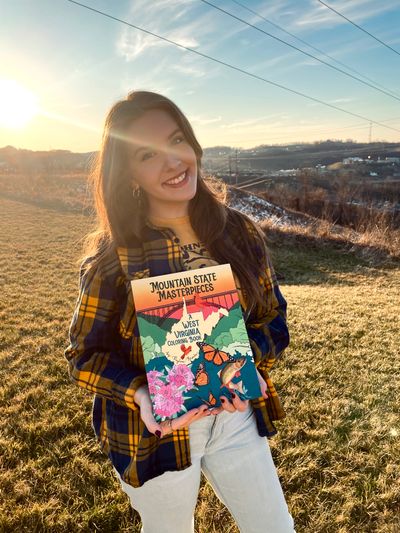 This is an image of Payton holding the first copy of my coloring book, Mountain State Masterpieces.