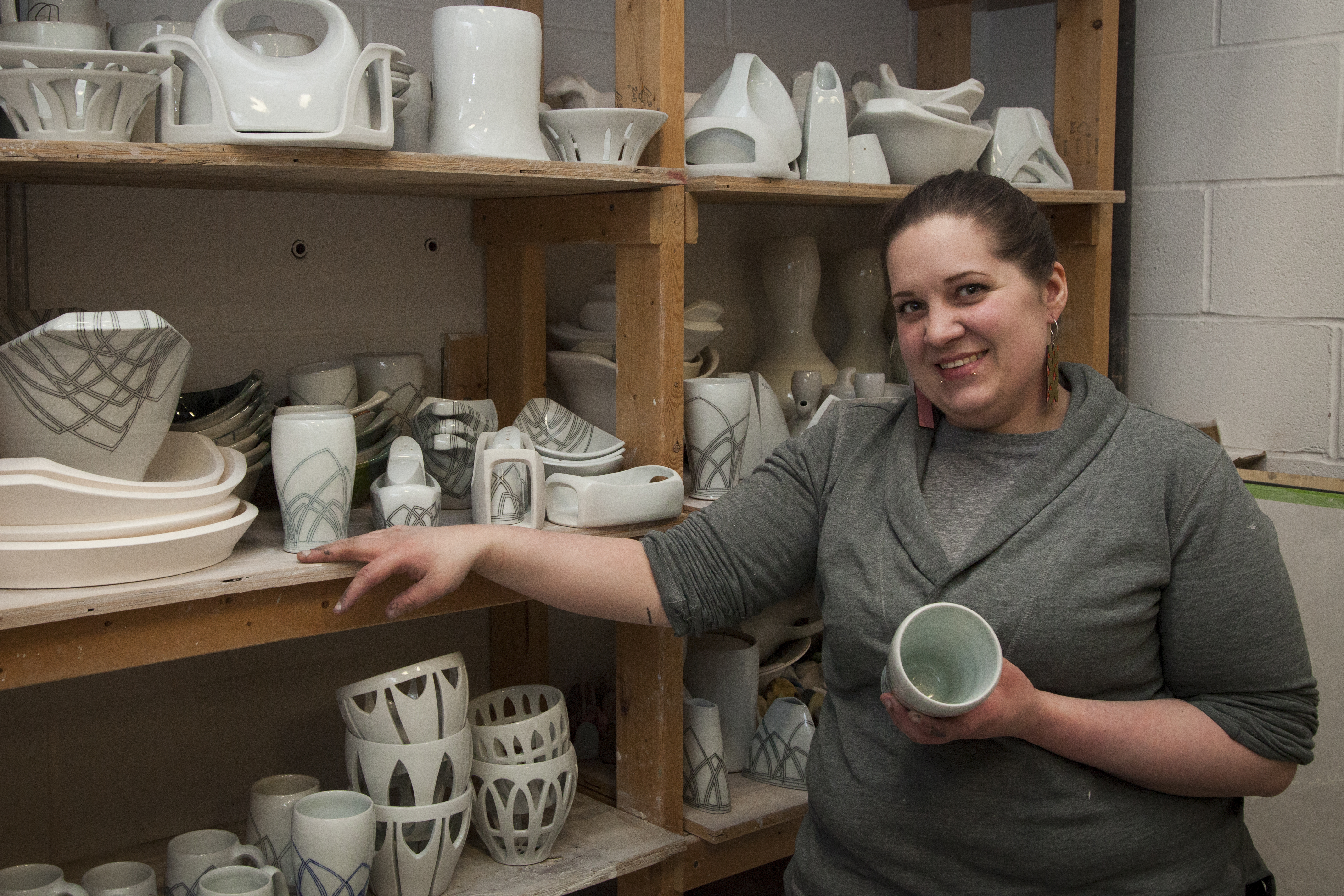 Art and design graduate student posing with their work in the ceramics studio